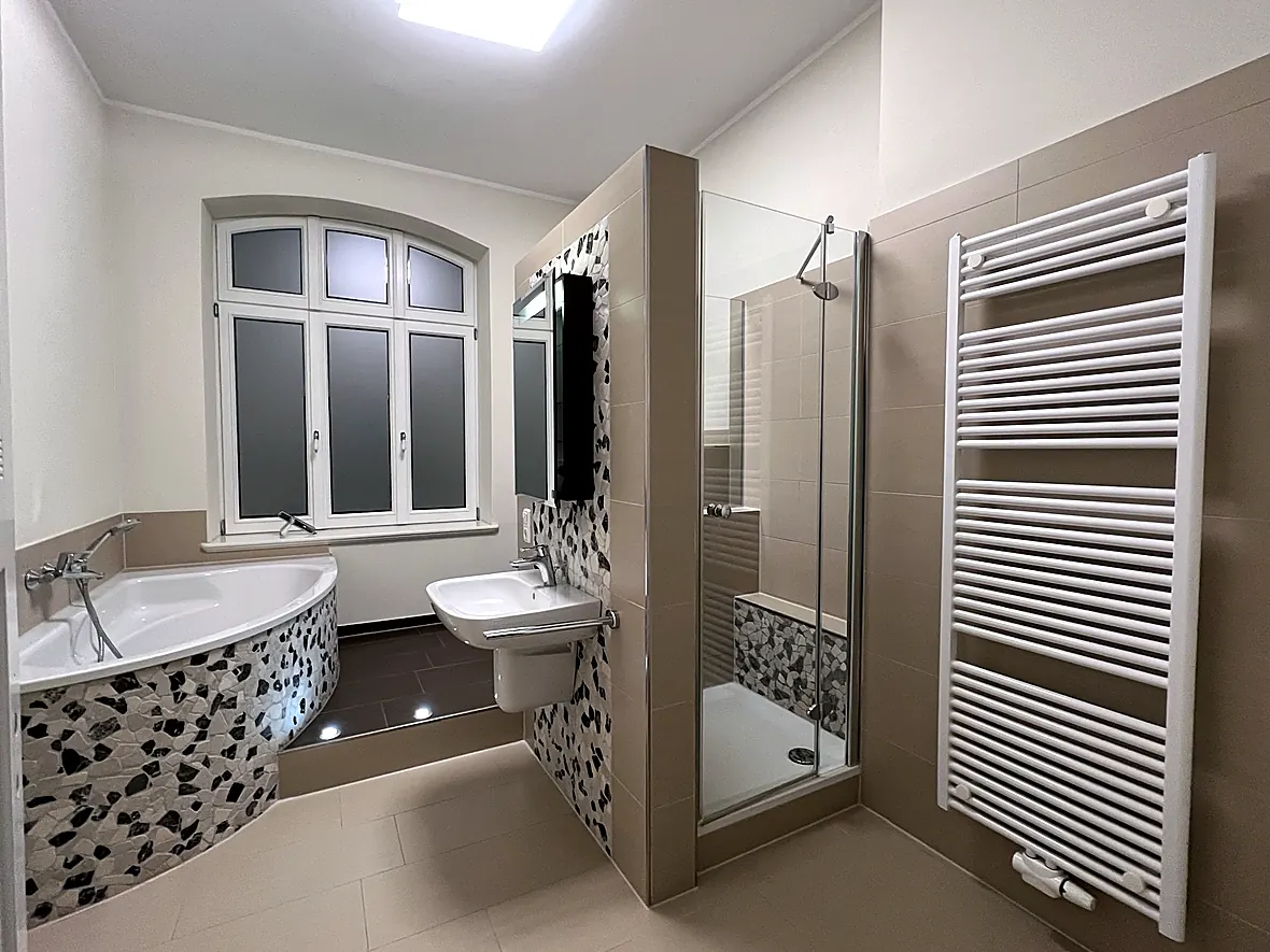 Modernes Bad der Villa Valentino mit Eckwanne, Natursteinmosaik, begehbarer Dusche, Podest mit Bodenspots und Handtuchheizkörper