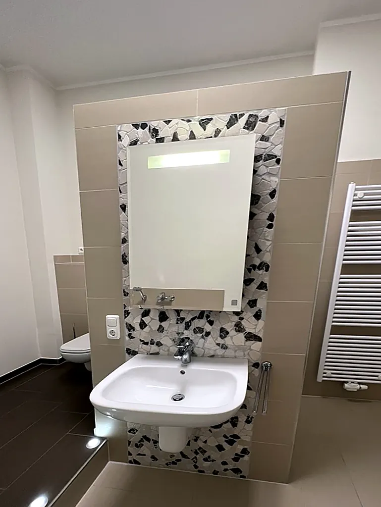 Waschbereich im Bad der Villa Valentino mit Mosaikwand, Spiegel, WC und Handtuchheizkörper