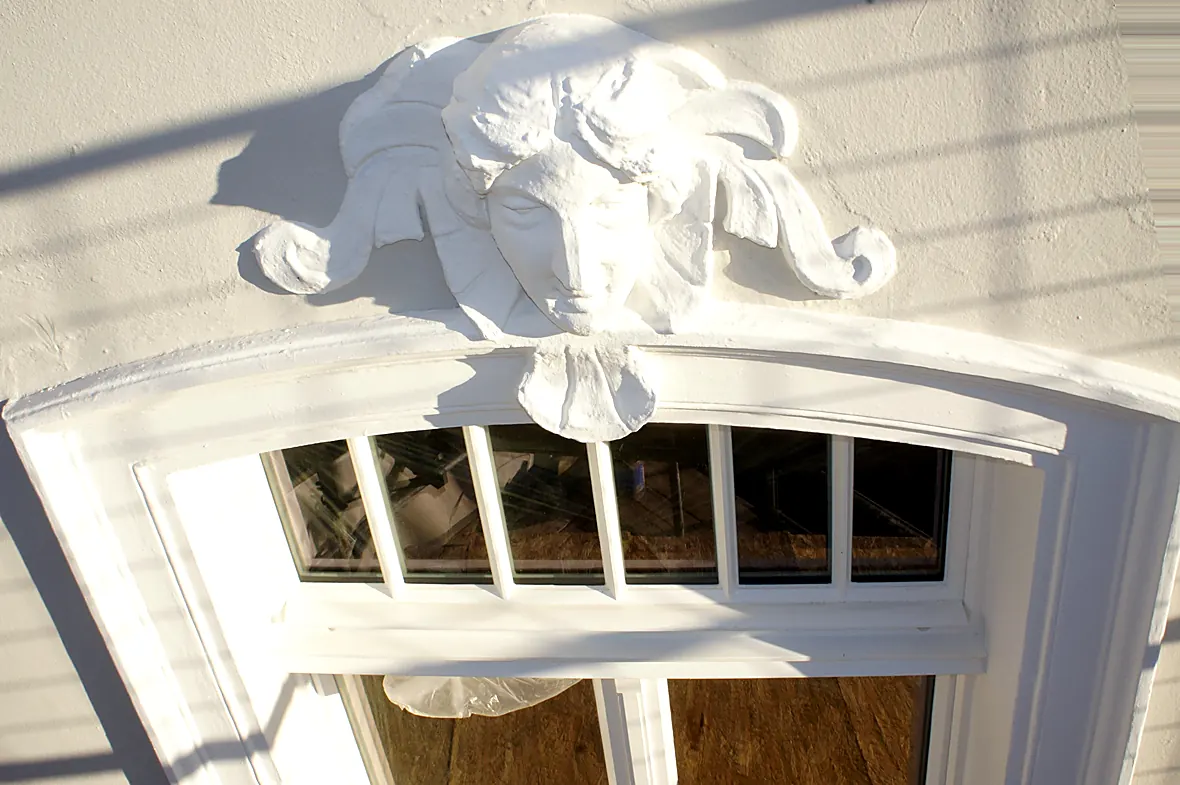 Restaurierter Engelskopf aus Stuck über einem Rundbogenfenster der Villa Valentino im Sonnenlicht