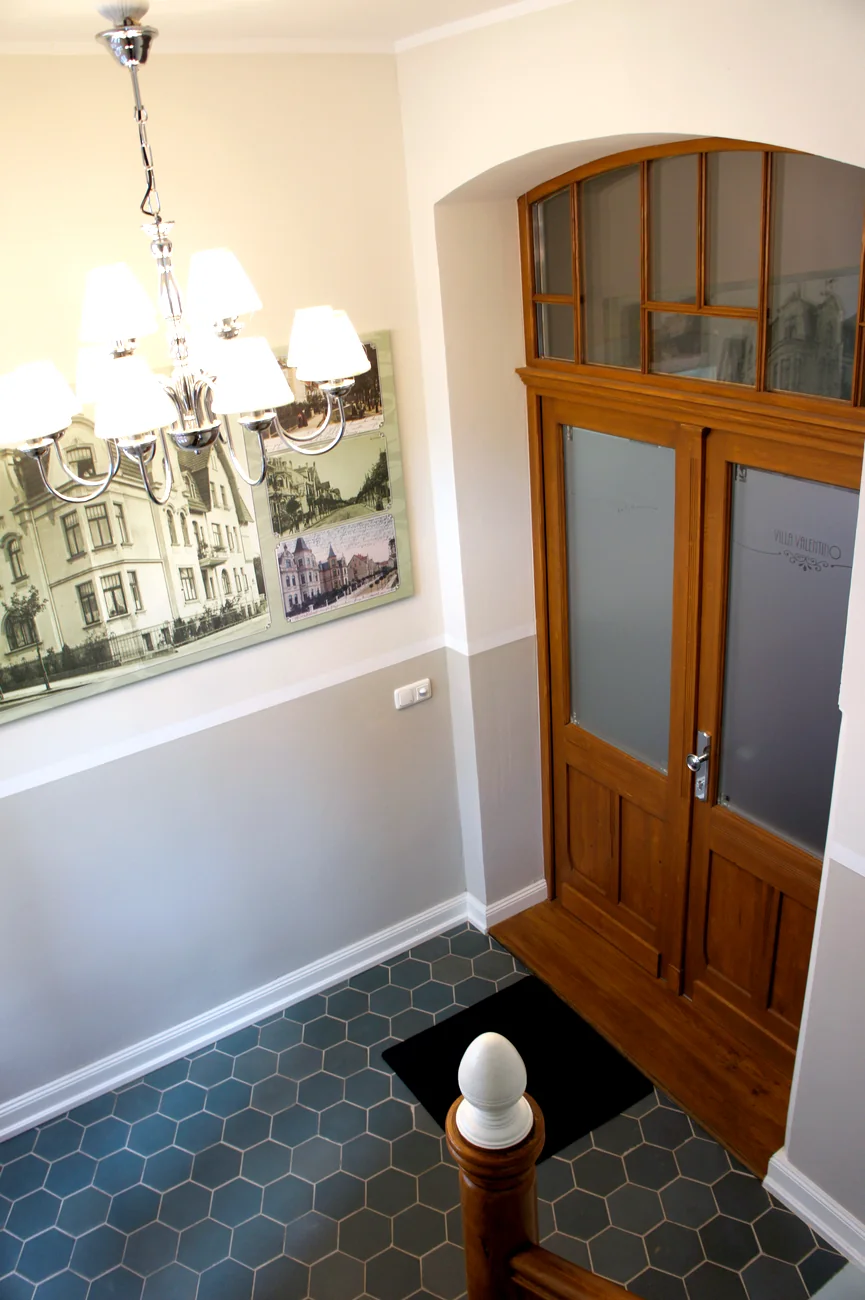 Foyer der Villa Valentino mit Kronleuchter, historischen Ansichtskarten von 1908 und der Ätzglastür mit Schriftzug Villa Valentino