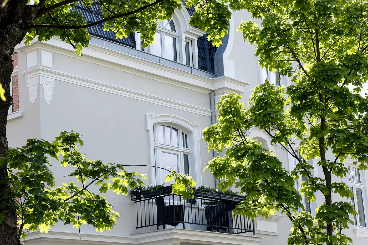 Villa Valentino in Bad Oeynhausen, eingerahmt von grünem Ahornlaub – sonnige Ansicht der sanierten Fassade mit Balkon und Schweifgiebel